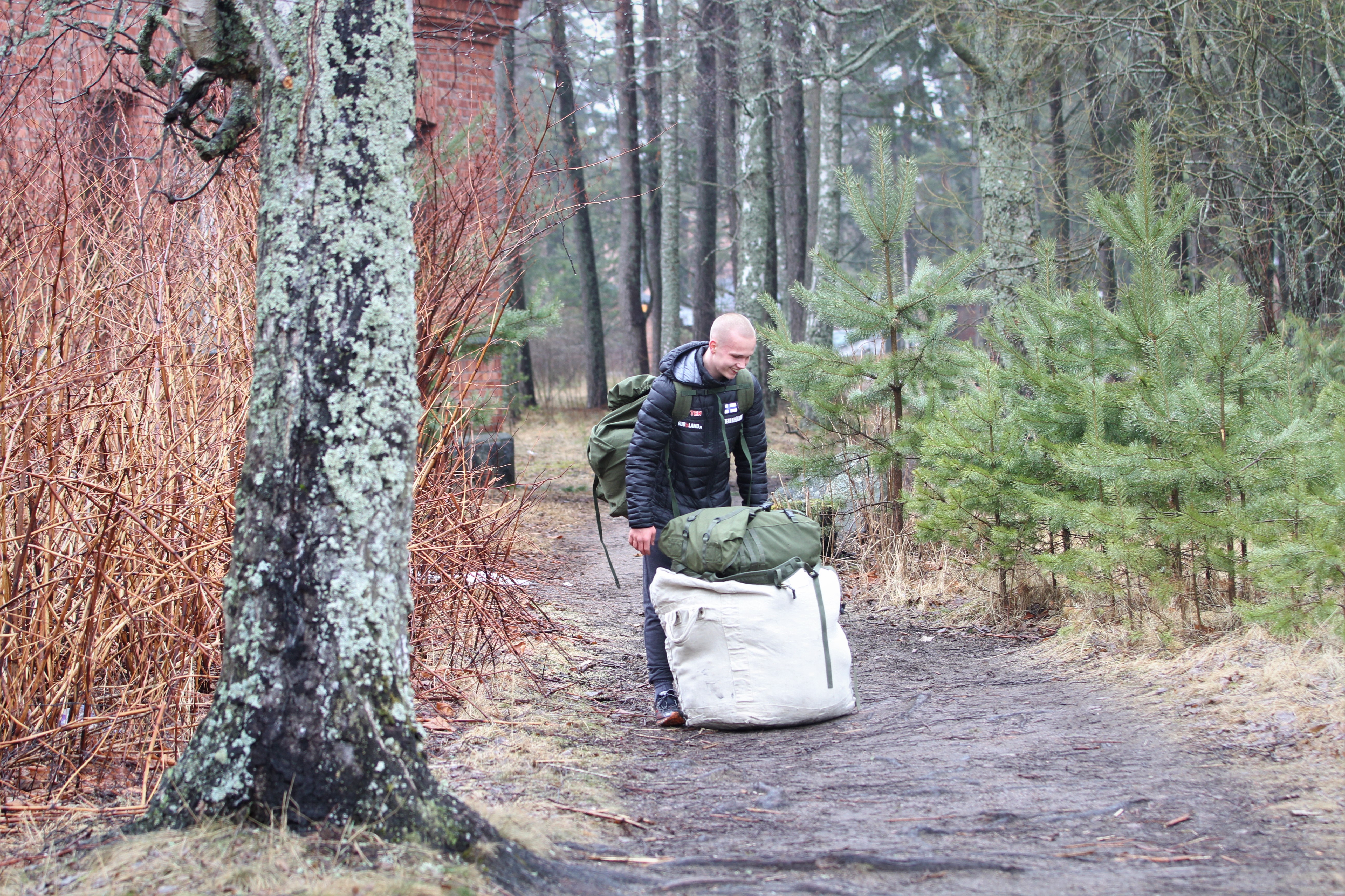 Mies hymyilee metsäpolulla kun on nostamassa varustesäkkiä