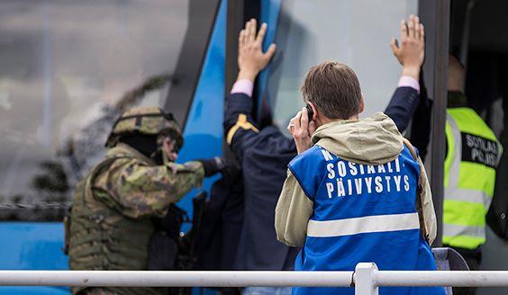 Military police deal with a civilian with his hands up. A person is talking on the phone, wearing a blue vest that says "Social Duty".