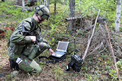 Sotilas käyttää tietokonetta ja radiota metsässä