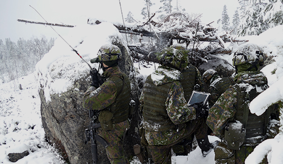 Sotilaita lumisessa metsässä isojen kivien suojassa