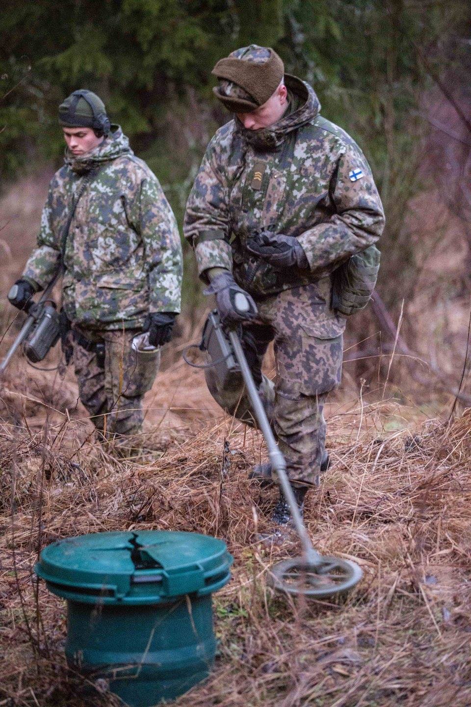 Two soldiers in the woods with metal detectors.