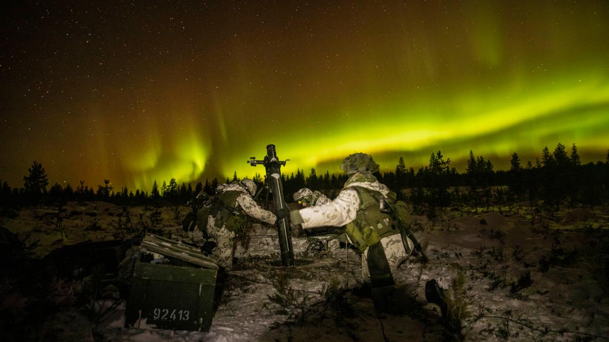 Vihreät revontulet halkovat taivasta, kun kranaatinheitinjoukkue valmistautuu ampumaan pimeässä talvimaisemassa.