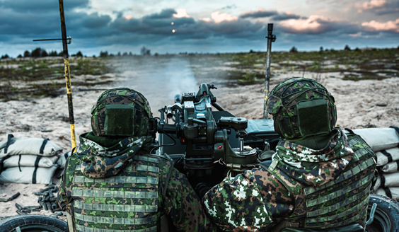 Keskellä kuvaa on kaksi varusmietä kuvattuna takaapäin, jotka ampuvat 23ITK61-ilmatorjuntakanuunalla. Lohtajan hietikolla. Kaukaisuudessa on pilvinen taivas.