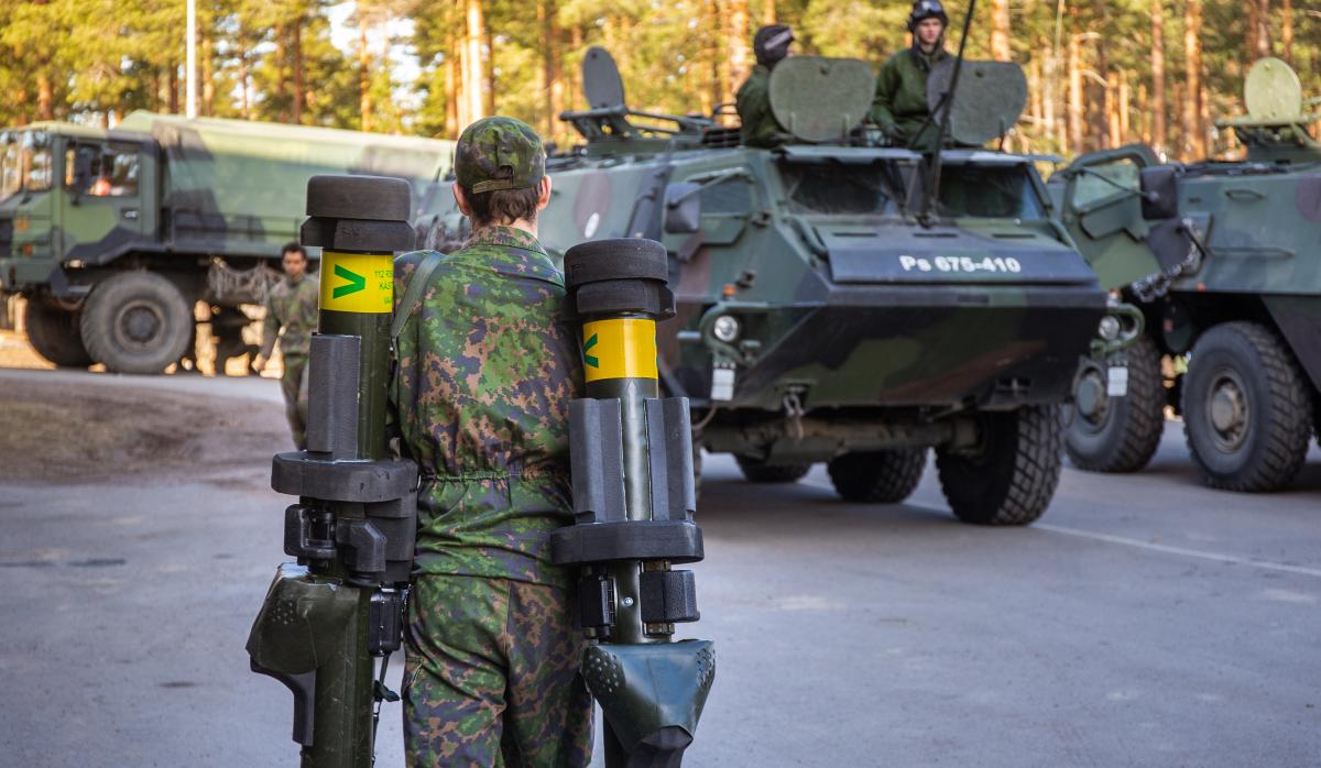 Sotilas kantaa kahta sinkoa kohti taustalla olevia panssaroituja ajoneuvoja.