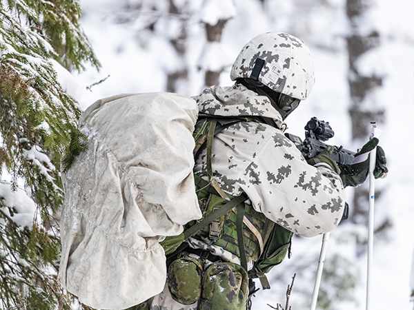 Sotilas suksilla lumisessa metsässä.