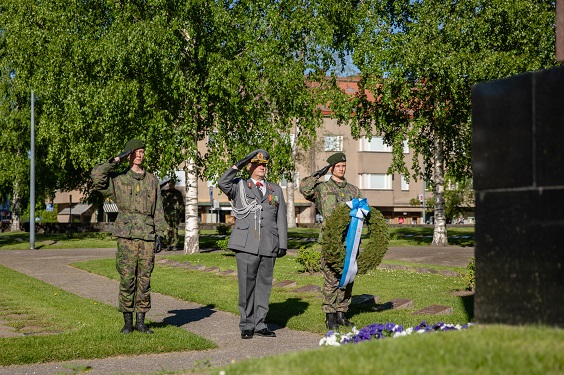 Seppeleenlasku, kolme sotilasta rivissä muistomerkin edessä, keskellä eversti harmaissa, sivuilla varusmiehet maastopuvuissa. Aurinko paistaa, kädet lipassa.
