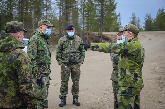 Kuvassa ruotsalainen sotilas maastopuvussa osoittaa kädellä, ympärillä suomalaisia sotilaita maastopuvussa.