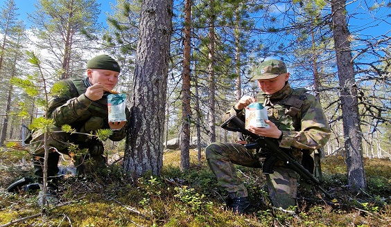 Kaksi soturia ruokailemassa pussista tyytyväisinä, aurinko paistaa ja sninen taivas.