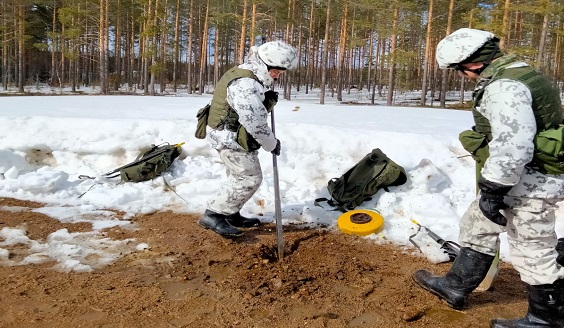 Kaksi lumipukuista sotilasta kaivaa paikkaa miinalle.