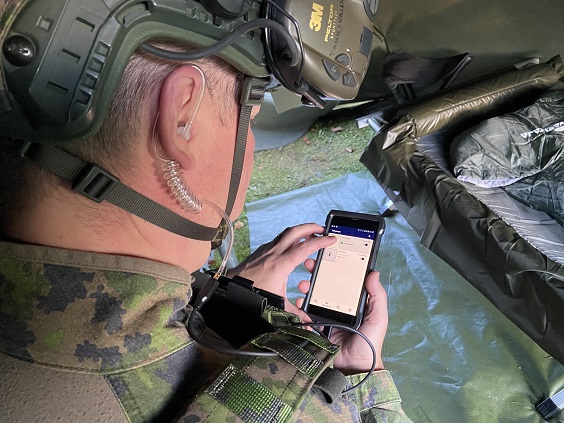 Sotilas maastopuvussa ja kypärässä kännykkä kädessään.
