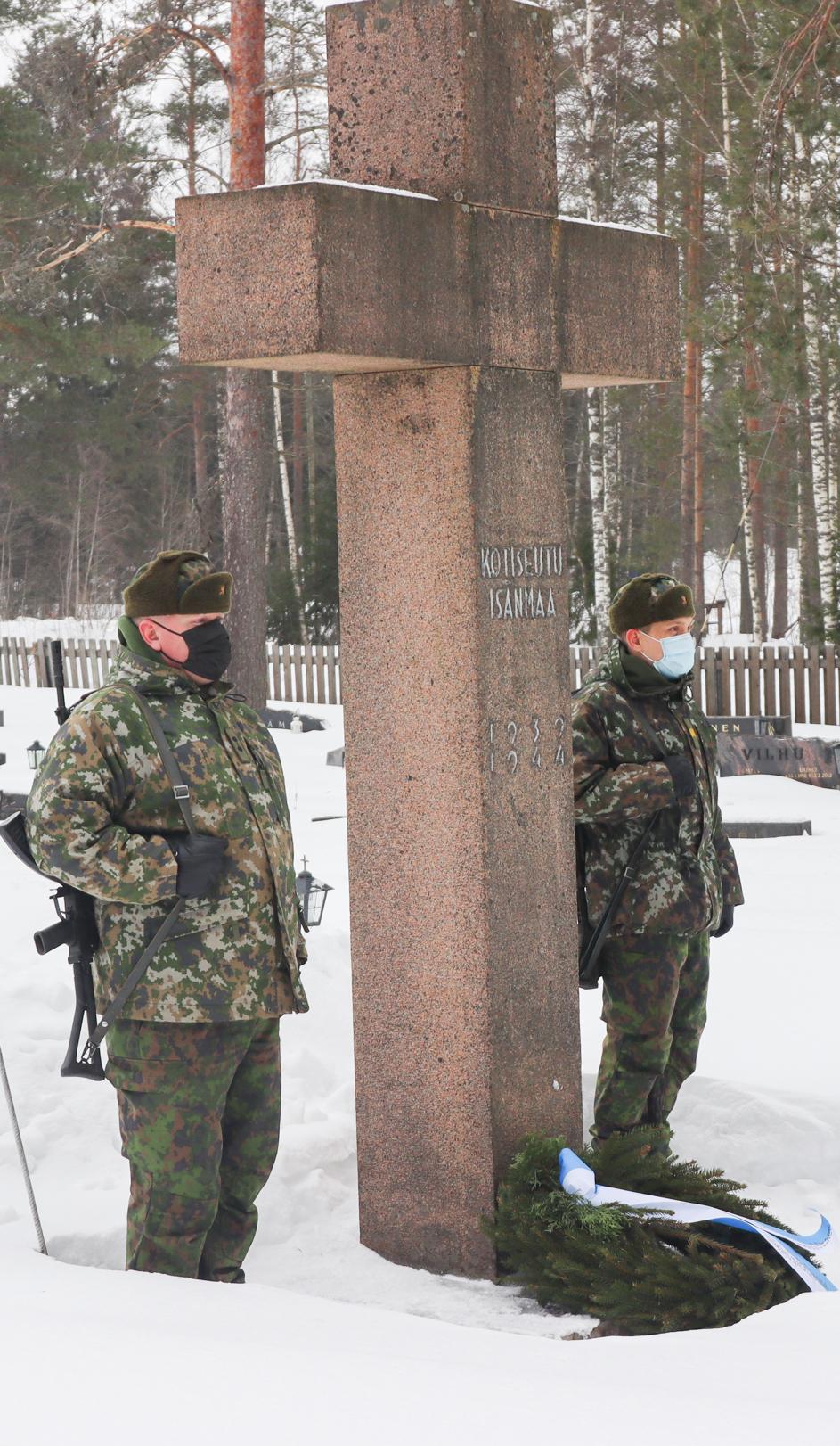 Kaksi sotilasta seisoo vartiossa hautausmaalla Kotiseutu, isanmaa -muistomerkillä, seppele on muistomerkin juurella.