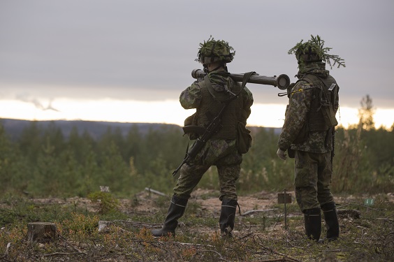 Kaksi maastopukuista sotilasta seisoo selin maastomaisemassa, toisella ilmatorjunta-ase olalla.