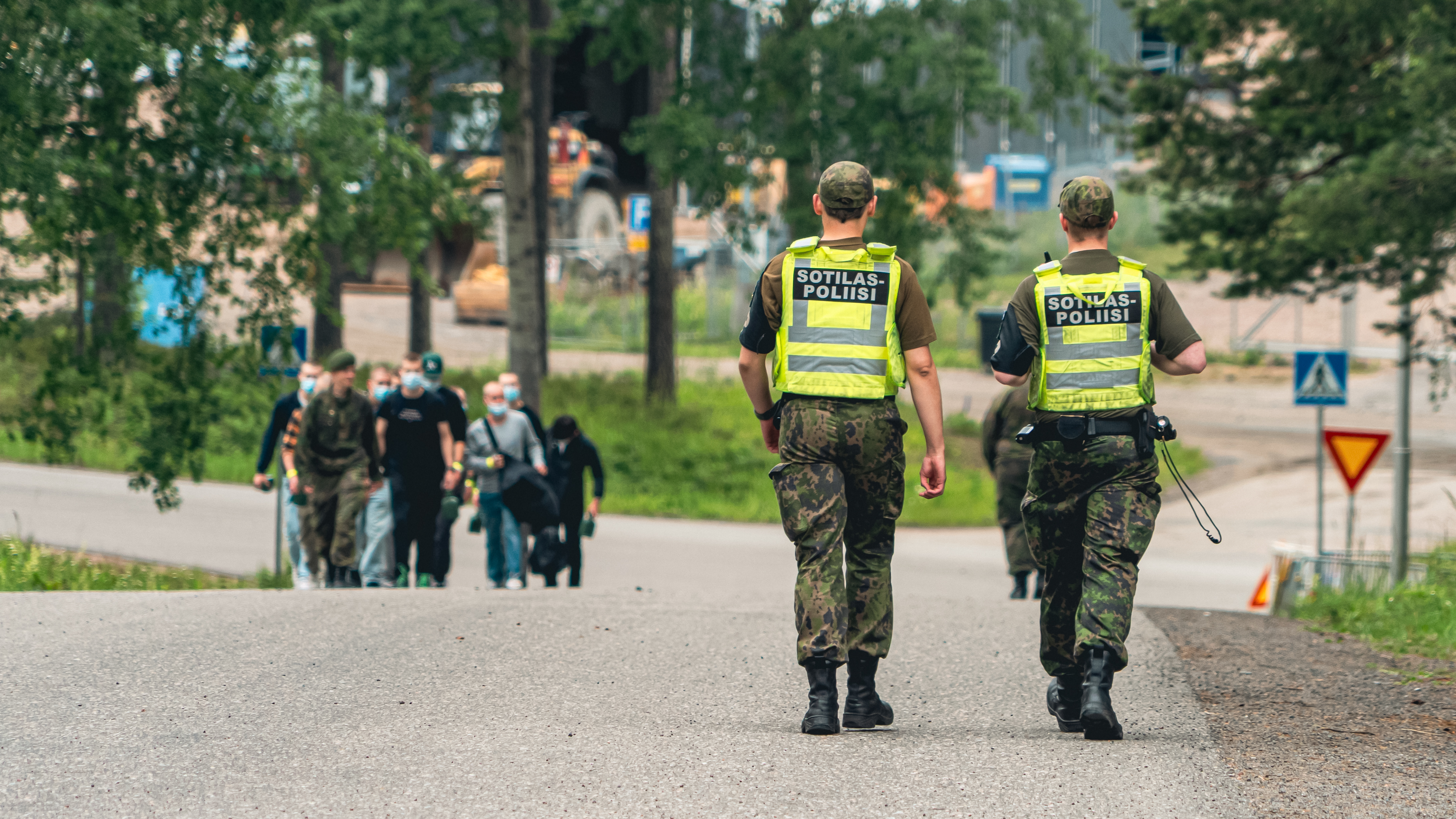 Sotilaspoliisit kävelemässä palveluksen aloittavien siviilipukuisten henkilöiden ohi varuskunnassa.