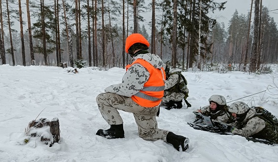 Sotilaita lumisessa maastossa. Yksi sotilaista on oranssissa kouluttajan liivissä: joukkueammunnan johtaja kadettikersantti Pohja valvoo joukkueen johtajan taistelunaikaista käskynantoa.