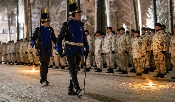 Perinteiden yö-hämärässä kaksi vanhoissa sotilaan asuissa olevaa sotilasta astelee lumipukuisten sotilaiden rivin edessä.