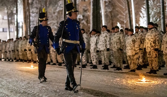 Perinteiden yö-hämärässä kaksi vanhoissa sotilaan asuissa olevaa sotilasta astelee lumipukuisten sotilaiden rivin edessä.