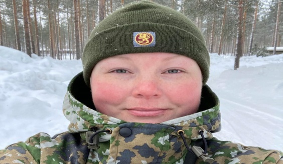 Punaiset posket ja hymy kasvoilla maastopukuisella reserviläisnaisella. Selfie-kuva.