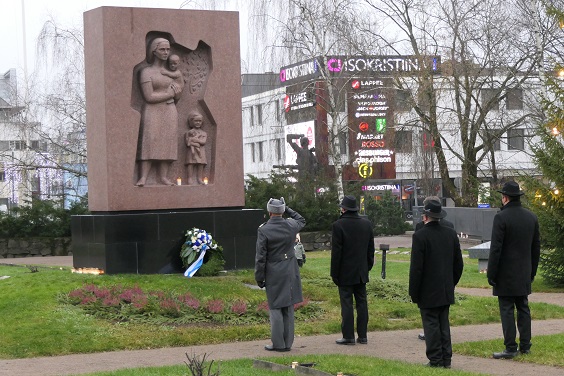 Sankarihautausmaan muistomerkki Lappeenrannassa, seppelettä laskemassa joukko ihmisiä, joista yksi sotilas harmaissa tekemässä sotilaallista kunniaa käsi lipassa.