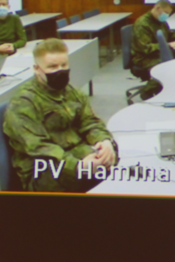 Näyttöruudulla maastopukuinen ja maskikasvoinen sotilas istuu ja osallistuu webinaariin.