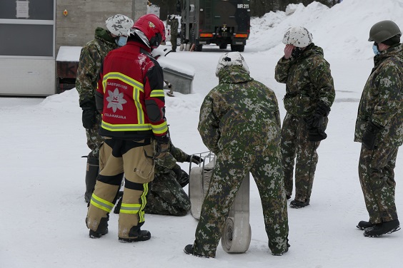 Pelastuslaitoksen punaisissa ja Puolustusvoimien maastokuvioisissa univormuissa yhdessä rullataan paloletkua talvisella palolaitoksen pihalla.