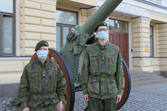 Kaksi varusmiestä seisovat maastopuvuissa ja kasvomaskeissa, taustalla näkyy muistomerkki-tykki.