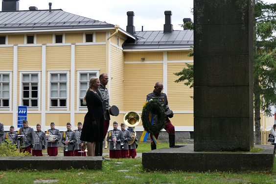 Seppeleenlasku Ratsuväen muistopatsaalla, kaksi rakuunapukuista sotilasta ja yksi siviili, taustalla näkyy rakuunapukuisia Rakuunasoittokunnan sotilaita.