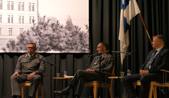 Kolme henkilöä (kaksi sotilasta, yksi siviili) istumassa rivissä ja keskustelemassa paikallispuolustuksesta.