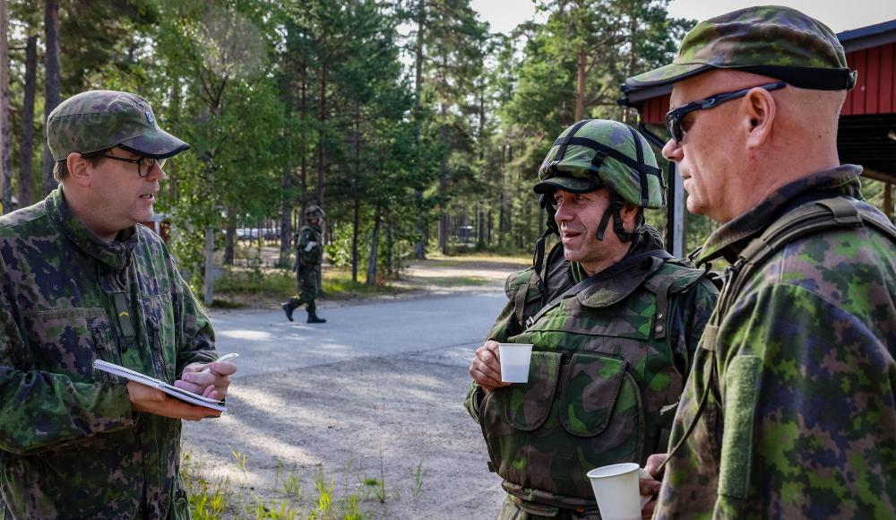 Kuvassa etualalla kolme reserviläistä joista viestinnän reserviläinen haastattelee kahta muuta kahvitauon aikana.