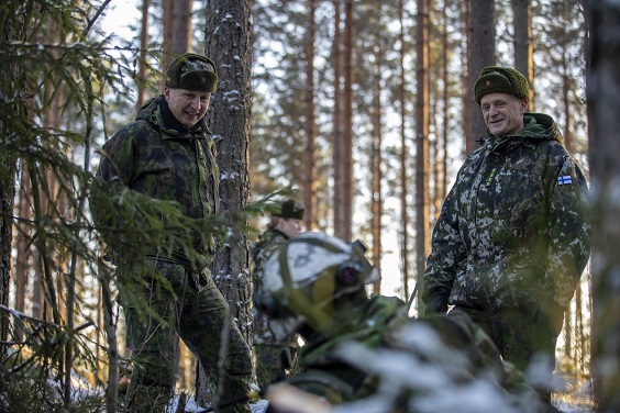 Maavoimien komentaja ja PV:n komentaja lumisessa maastossa hymyssä suin juttelemassa varusmiehen kanssa, joka on maastoutunut maahan ja selin.