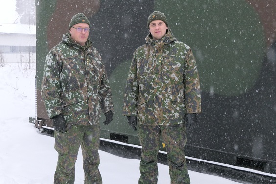 Kaksi maastopukuista sotilasta maastokuvioiden esikuntakontin edessä lumipyryssä.