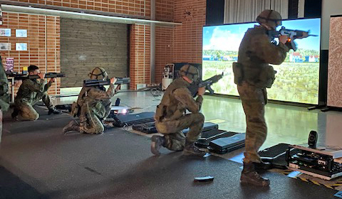 Neljä sotilasta ampuu simulaattoriaseilla, yksi seisaaltaan rynnäkkökiväärillä, kolme polvillaan kevyellä kertasingolla.