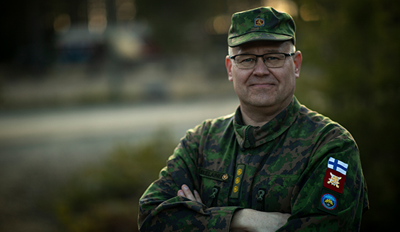 Ilmatorjunnan tarkastaja katsoo kameraan. Taustalla sumea metsäinen maisema.
