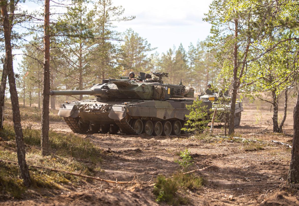 Kuvassa kaksi Leopard 2A6 -taistelupanssarivaunua alkukesäisessä maisemassa hiekkaisessa kangasmaastossa.