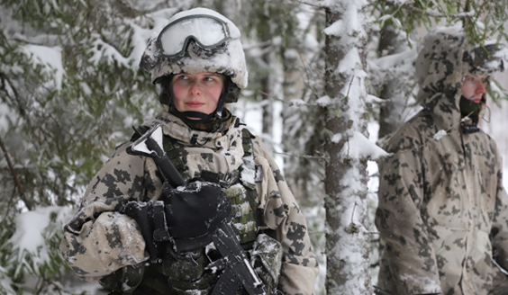Naisvarusmies seisoo lumipuvussa metsässä lumisessa maisemassa ja hymyilee.