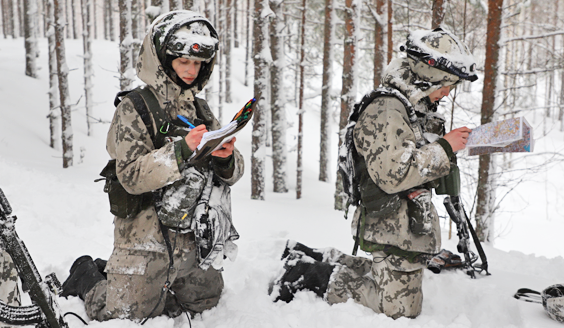 Kaksi lumipukuista upseerioppilasta katsoo karttoja lumihangessa.