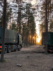 kaksi vihreää kuorma-autoa metsässä, aurinko nousee horisontissa