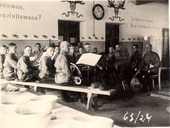 Historiallinen mustavalkoinen kuva, jossa pöydän ääressä istuu sotilassoittajia.