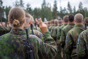 Sotilaspuvuissa rivissä olevat henkilöt kuvattu takaapäin. Jokaisella nostettuna etu ja keskisormi pystyyn.