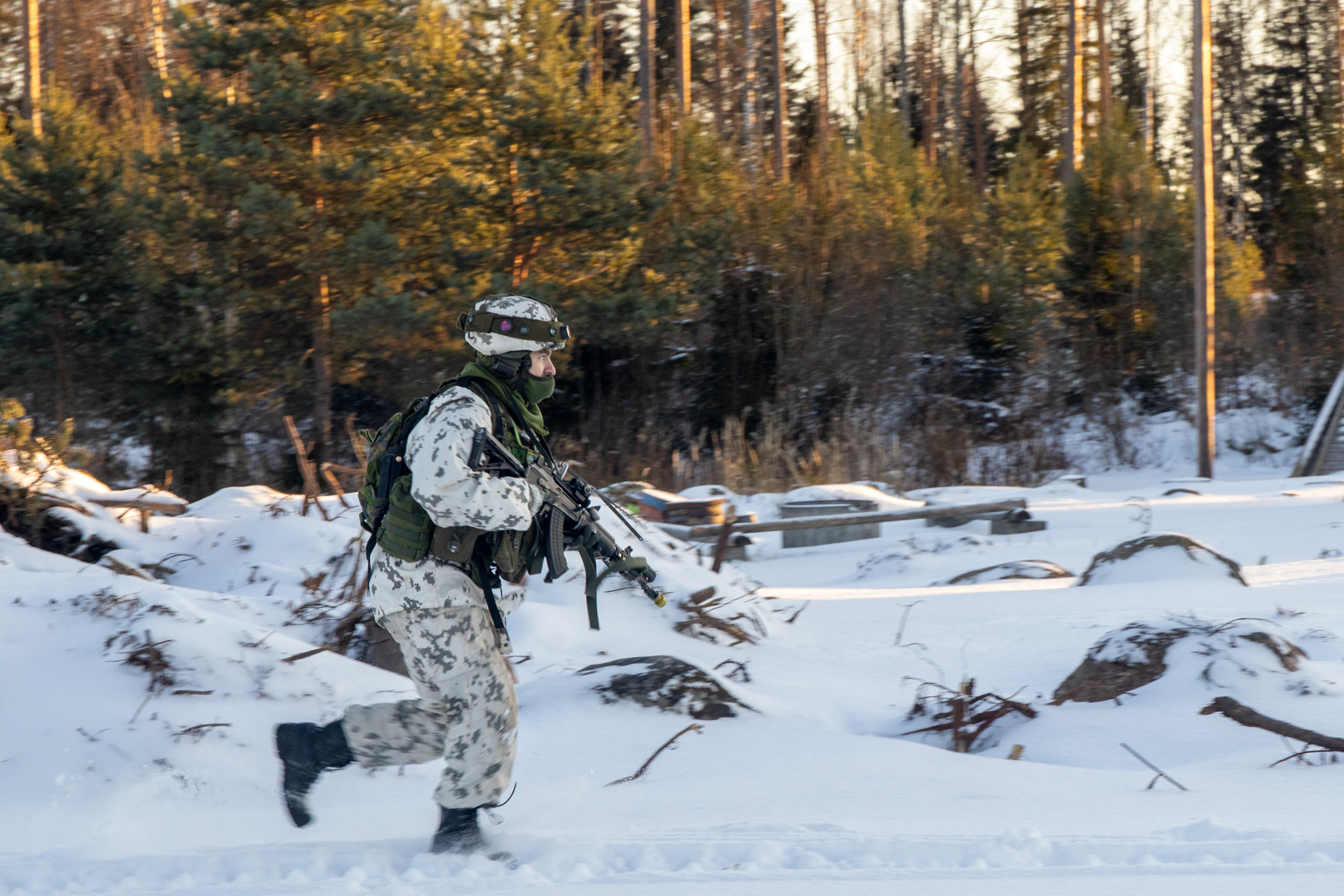 Talvipukuinen sotilas juoksee maastossa ase edessä valmiina ampumaan.