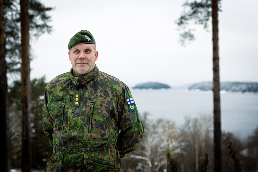 Everstin arvoinen sotilas ulkona maastopuvussa järvimaiseman edessä.