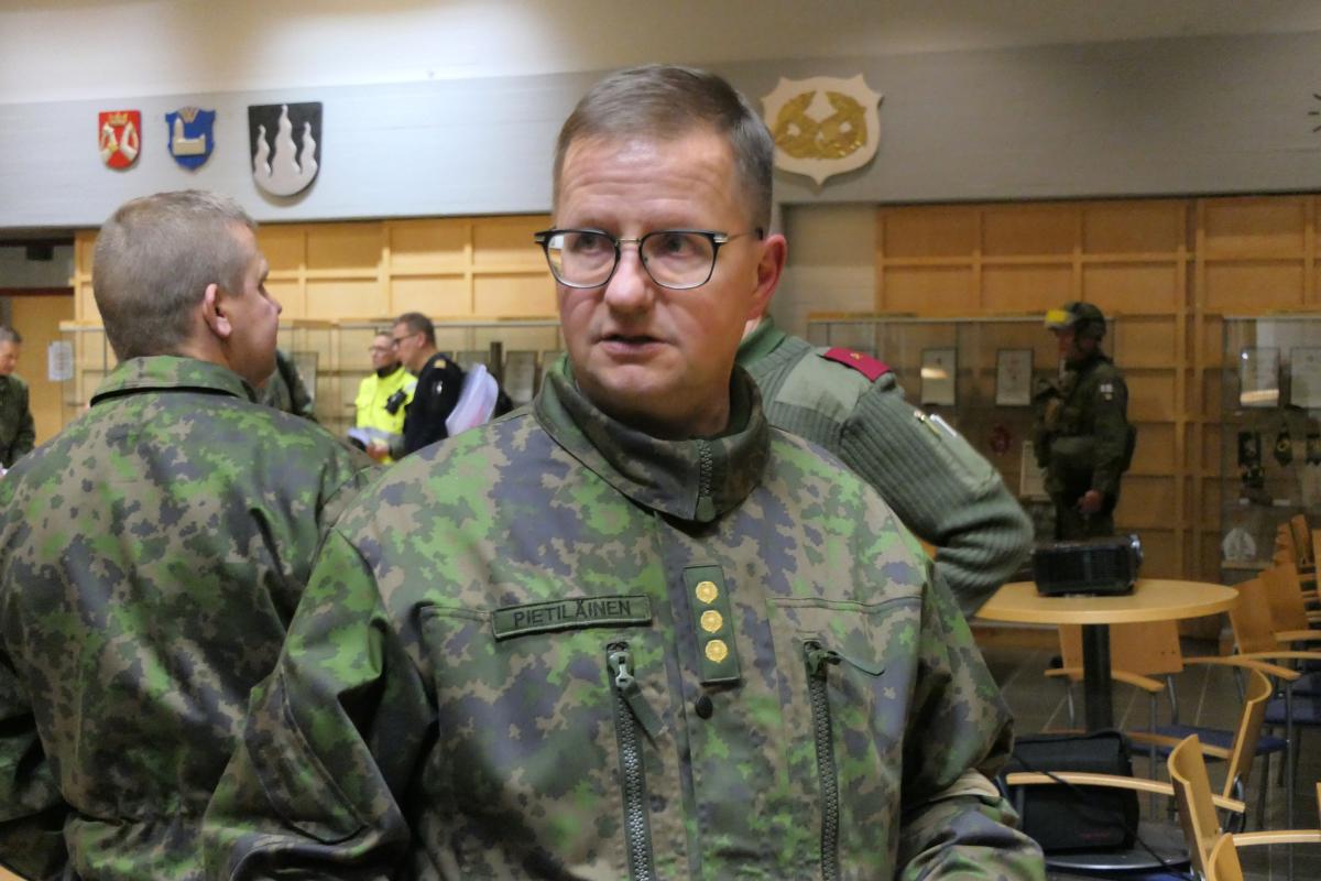 Kuvassa eversti Pietiläinen. Taustalla näkyy muita ihmisiä ja seinällä Karjalan prikaatin joukko-osastotunnus.
