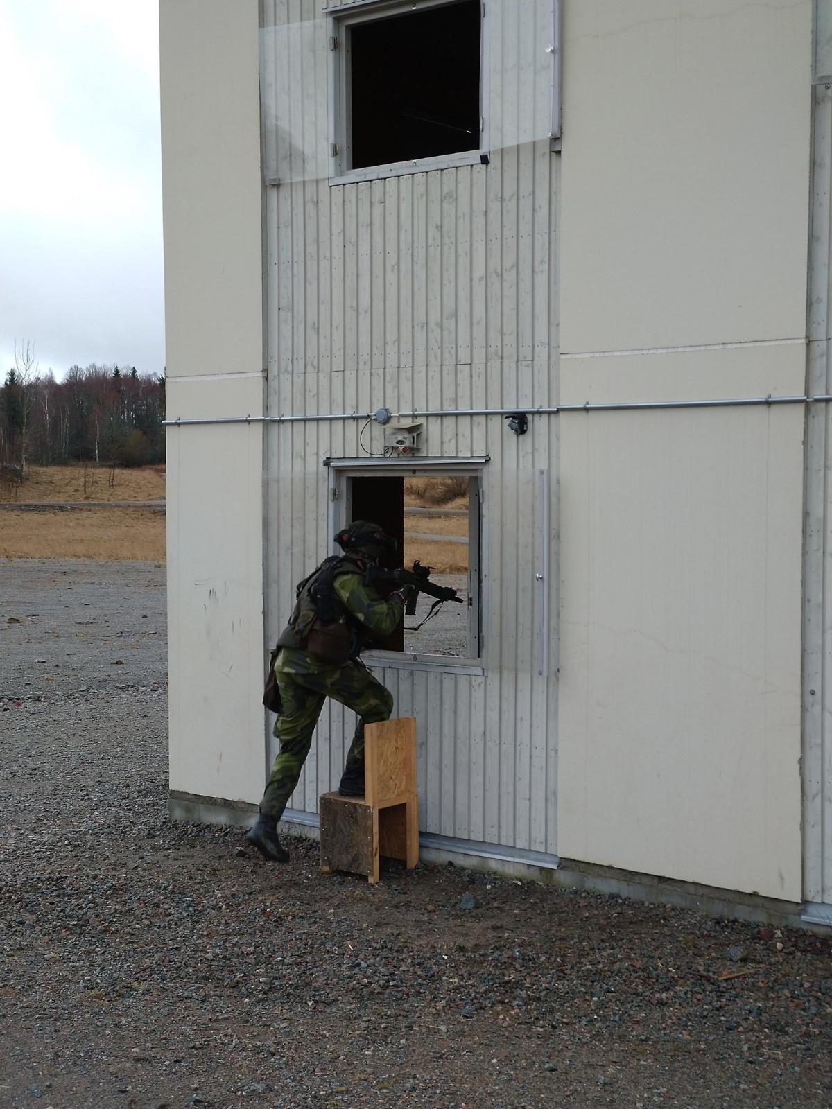 Kuvassa ruotsalainen kadetti tähtää aseella seisoma-asennossa seinän vieressä.