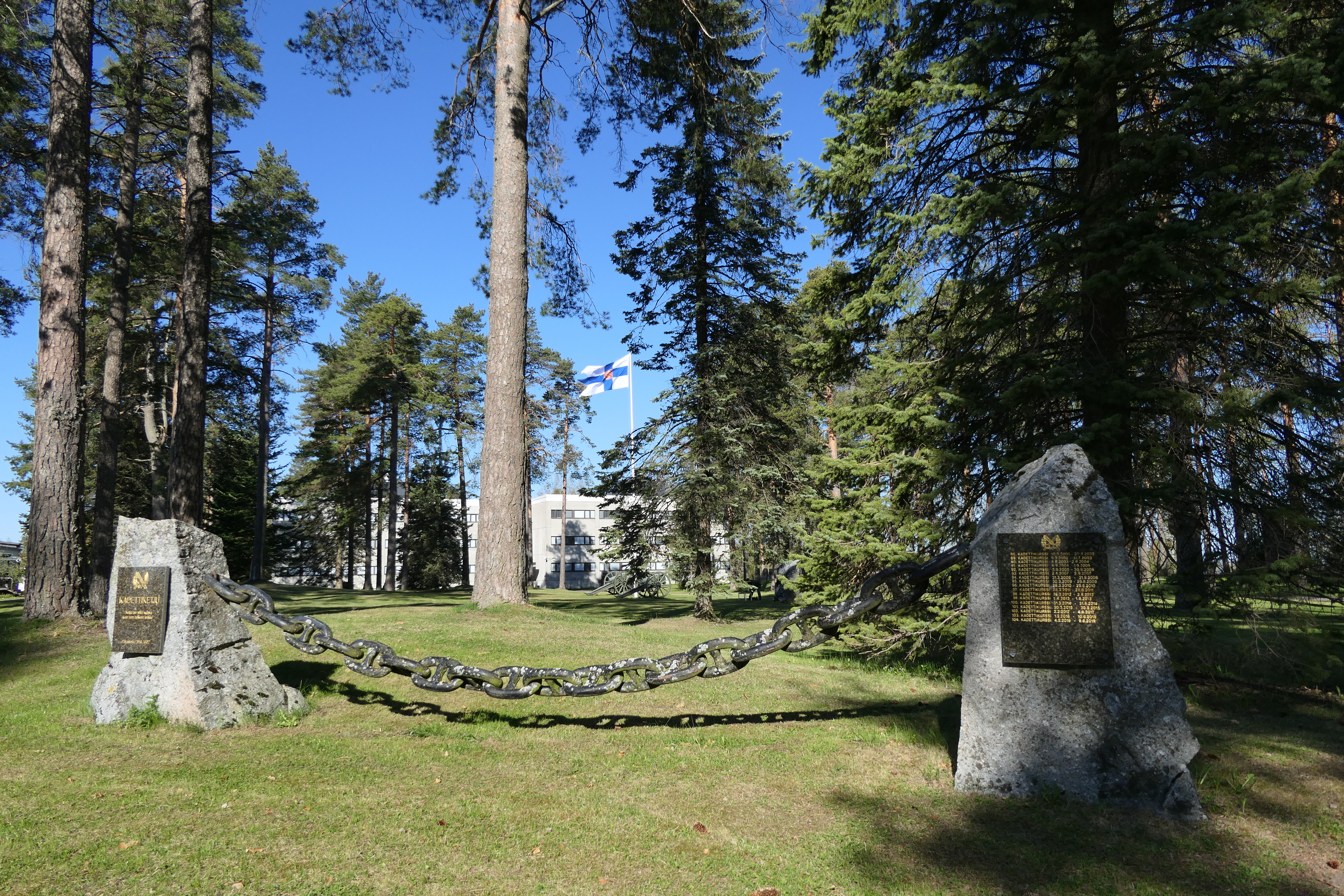 Vehreä Vöyrin puisto Lappeenrannan varuskunnassa. Etualalla kadettiketjumuistomerkki. Taustalla PV:n lippu.