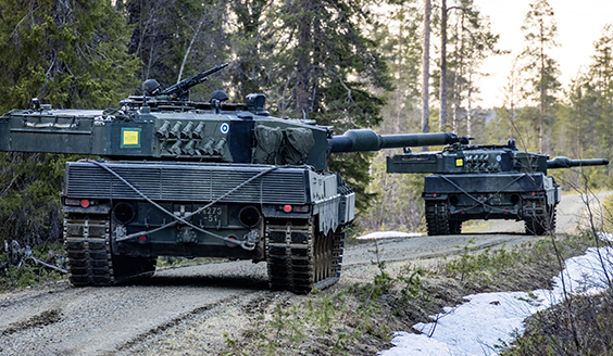 Kaksi panssarivaunua ajamassa peräkkäin hiekkatiellä maastossa.