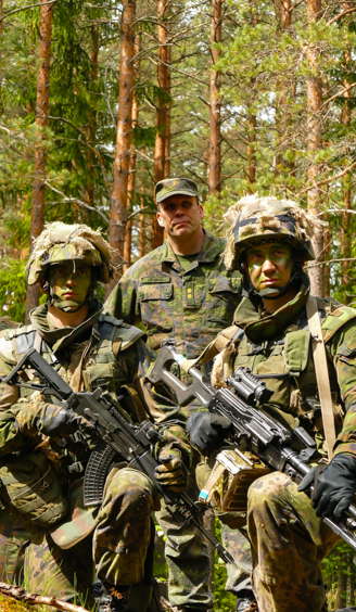 Kolme sotilassta seuraa koulutusta metsämaastossa.
