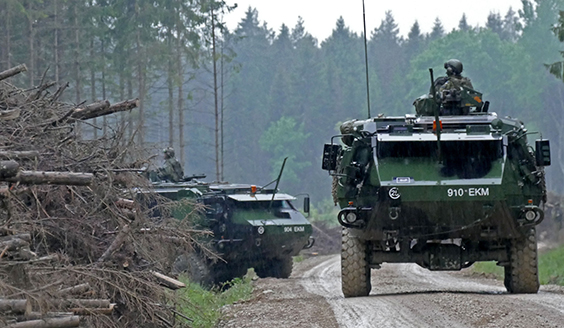 Kuvituskuva, jossa näkyy kaksi Suomen kansainvälisen valmiusjoukon varusmiestä kahden panssariajoneuvon tähystysluukusta hiekkatiellä harjoituksessa Virossa.
