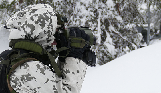 A soldier looks through binoculars at snowy terrain