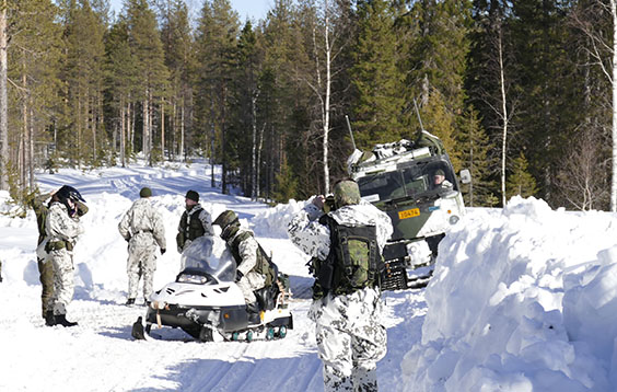 Tela-ajoneuvo, sotilaita ja moottorikelkka lumisella metsätiellä