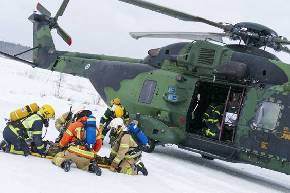 Palomiehet valmistautuvat nostamaan paareilla makaavaa sotilasta. Taustalla helikopteri.