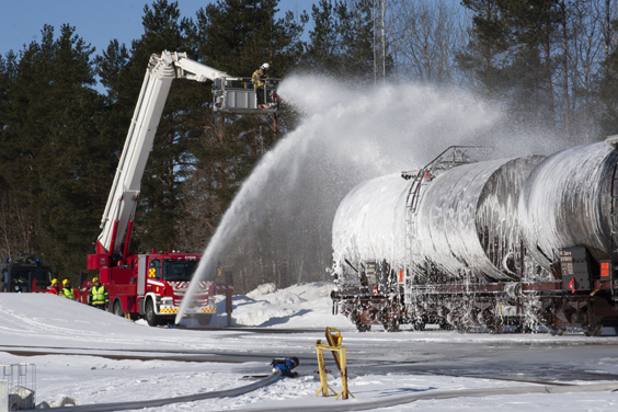 Palomies suihkuttaa vaahtoa säiliöjunanvaunujen päälle paloauton nosturista käsin